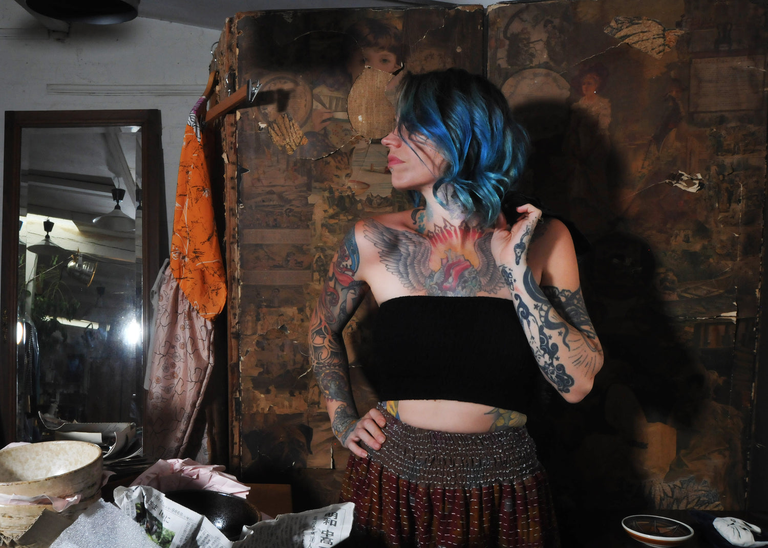 Model standing against a vintage wardrobe looking away from camera with blue hair and wearing vintage palazzo pants 