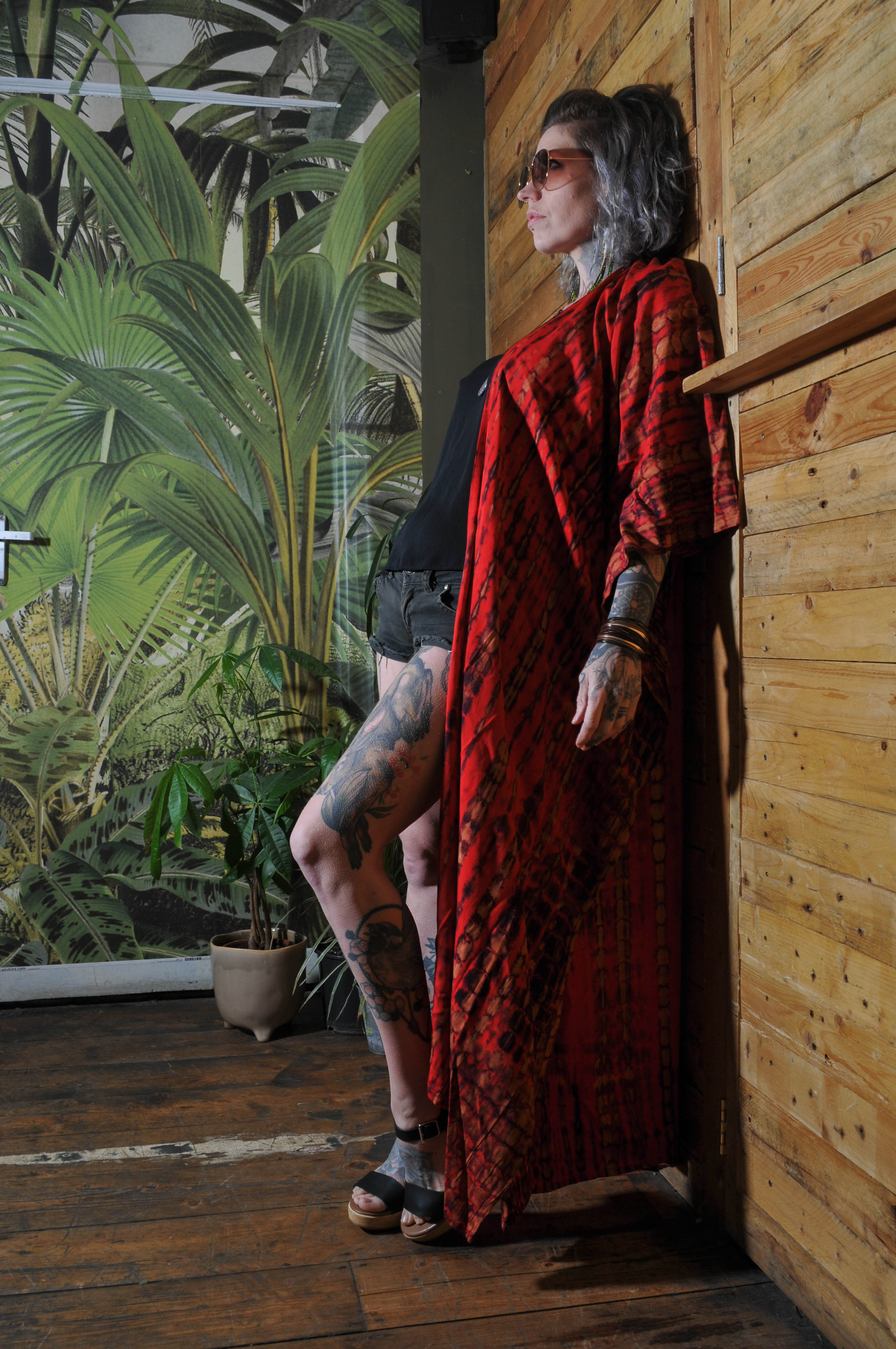 Model standing against a wooden bar room wall with botanical prints and wearing a red and black tie dye kimono 
