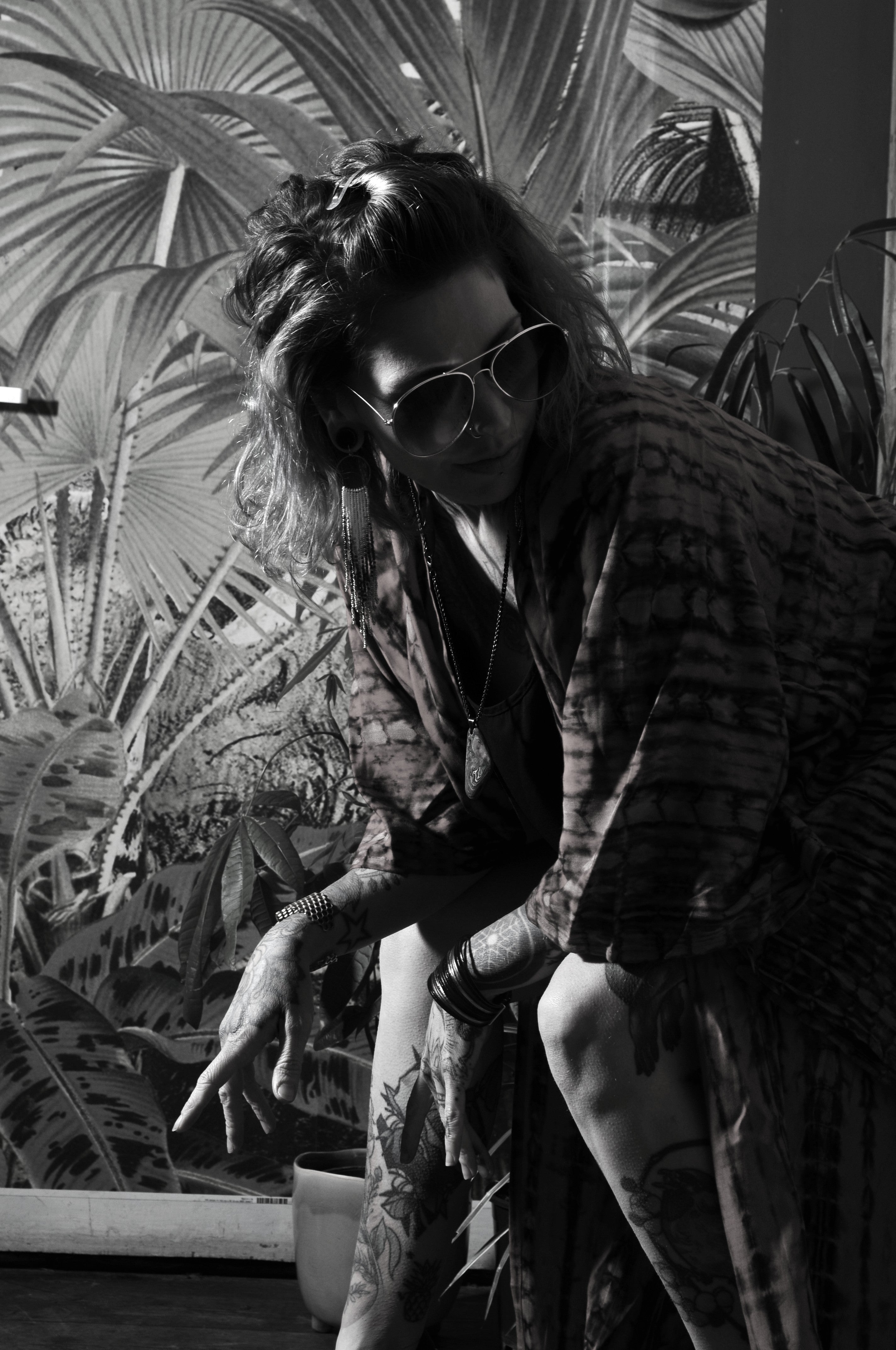 Black and white photo of model wearing a tie dye kimono against a botanical backdrop in a bohemian vintage bar 